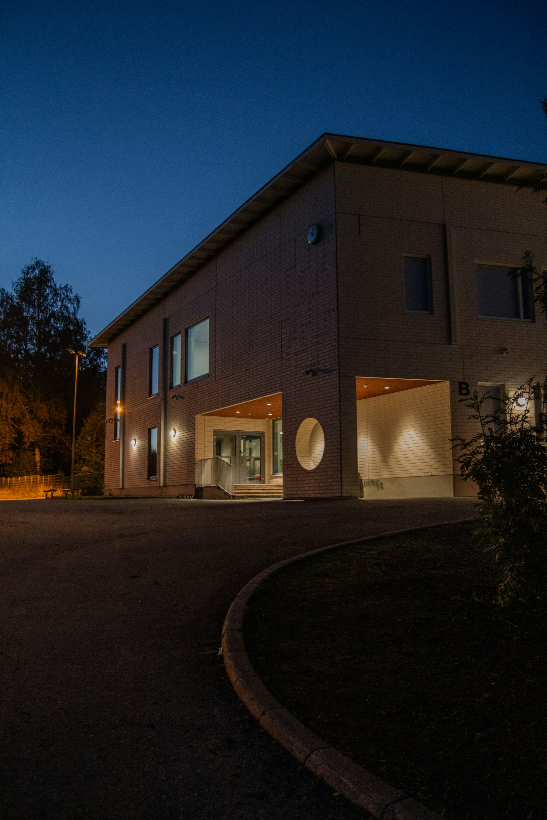 Entree van een modern zorggebouw in het blauwe uur, met warm licht binnen